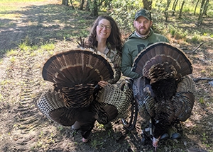 Hunter in wheelchair and their hunting partner show off their turkeys.