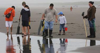 What appears to be two families stand close to each other on a wet beach looking for clams
