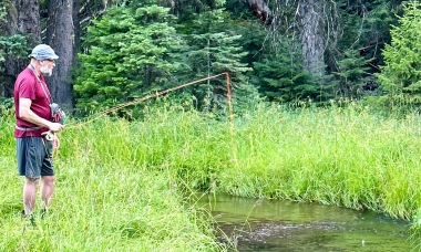 An angler stands on the grassy bank casting to a tiny stream