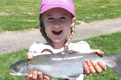 A happy girl uses two hands to holds a large trout out to the camera